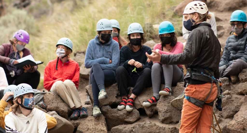 an outward bound instructor gives direction to a students preparing to rock climb